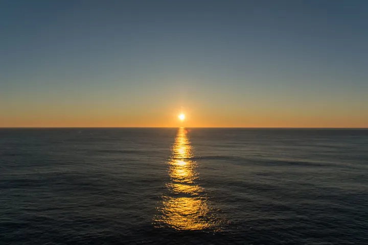 Le soleil bas posé sur un horizon vide, sa traînée dorée descendant jusqu’au bas du cadre sur une mer sombre.
