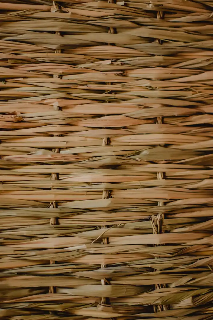 Une natte de lames de palme tressées à plat, brins beige et rosé serrés les uns contre les autres, en gros plan.