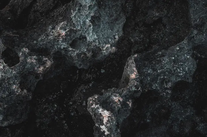 De la roche volcanique noire en gros plan, criblée de cavités, avec des éclats cuivrés au fond des creux.